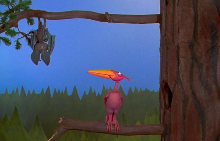 A Claymation bat hangs from a tree branch, watched by a large brightly-coloured bird on the branch below.